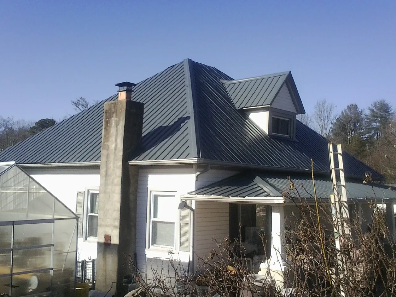 Dark blue standing seam metal roof on a white farmhouse with dormer — Slate & Tile Roof Repair by Roofing Brothers in Boulder City