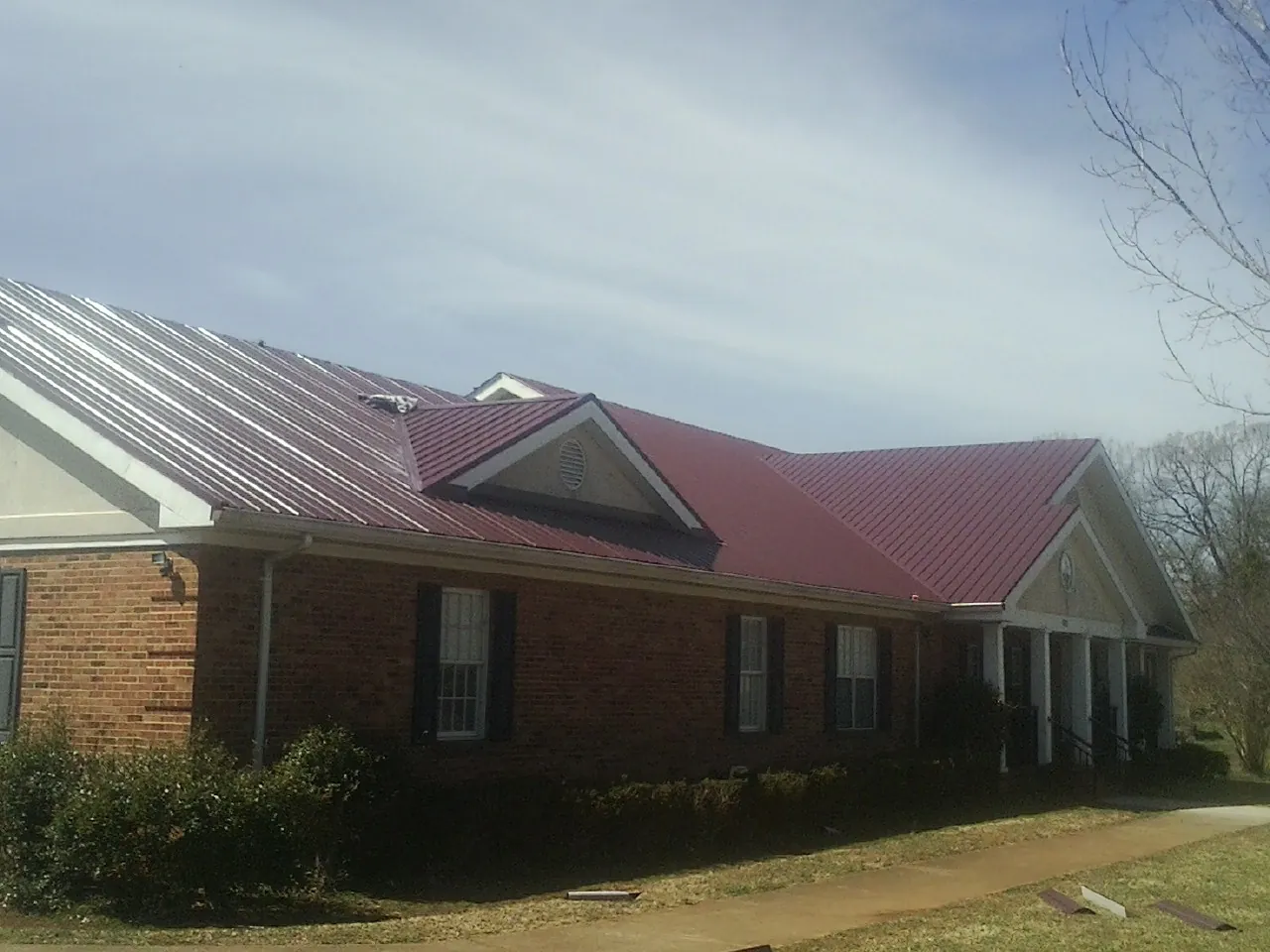Red metal roof with gabled entries on a long brick building, from a Hail Damage Roof Repair job in Boulder City