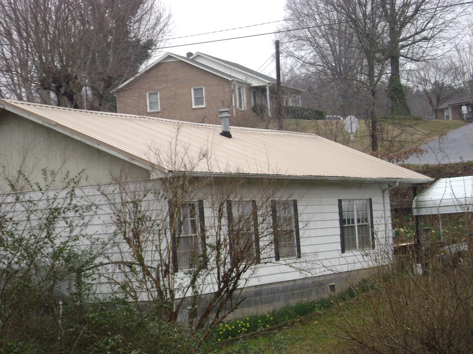 Tan metal roof on a white sided house set into a hillside — Commercial Roofing by Roofing Brothers in Boulder City